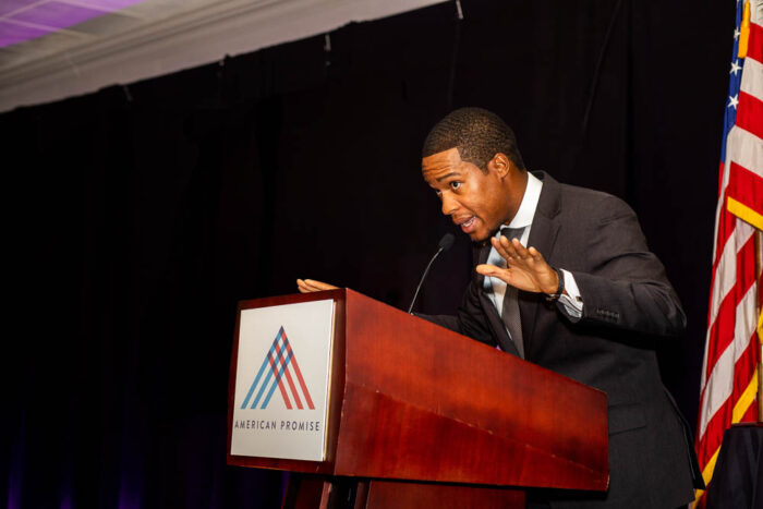 a man speaking at an American Promise podium