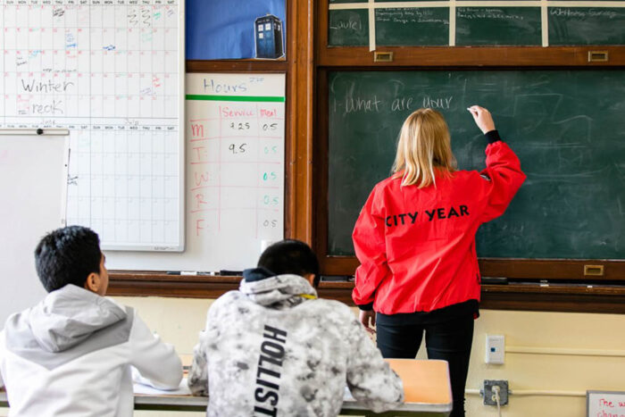 city year volunteer writing on a chalkboard in front of a class