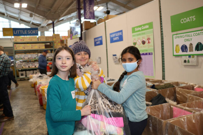 three young volunteers holding a bag of donated clothes