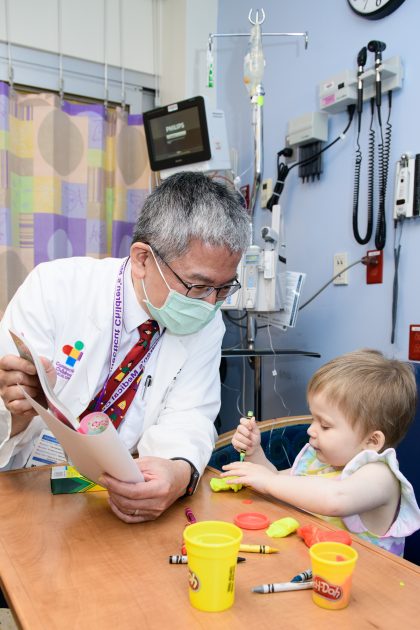 doctor talking a with a child in a hospital bed playing with crayons