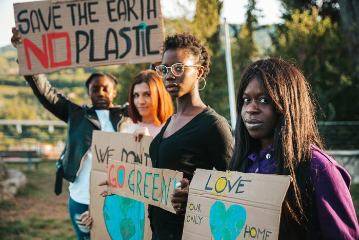 four omen holding signs that say go green and save the earth no plastic