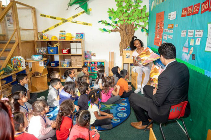 two adults reading to a group of children 