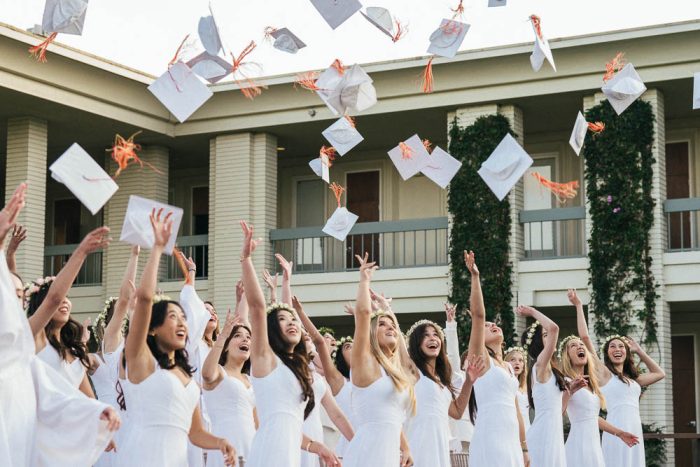 group of teenage girls dressed in white throwing graduation caps in the air
