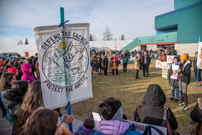 group of people and a sign tat says defend the sacred protect the arctic