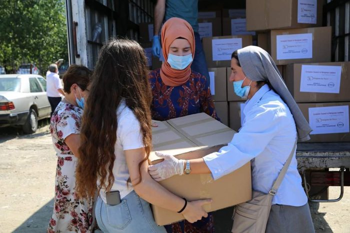 a woman in a hijab and a nun working together to lift a box