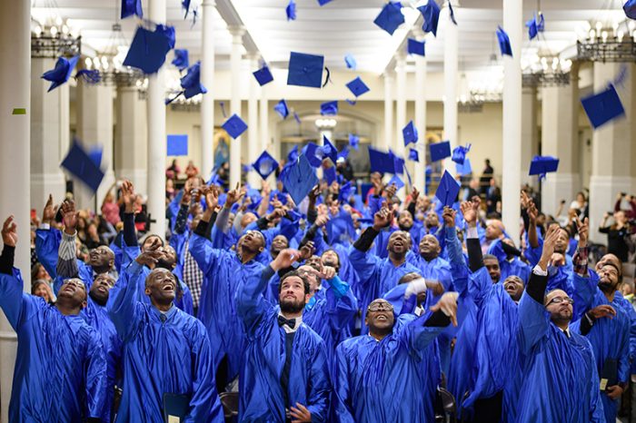 group of graduates in blue robes and tossing blue caps in the air